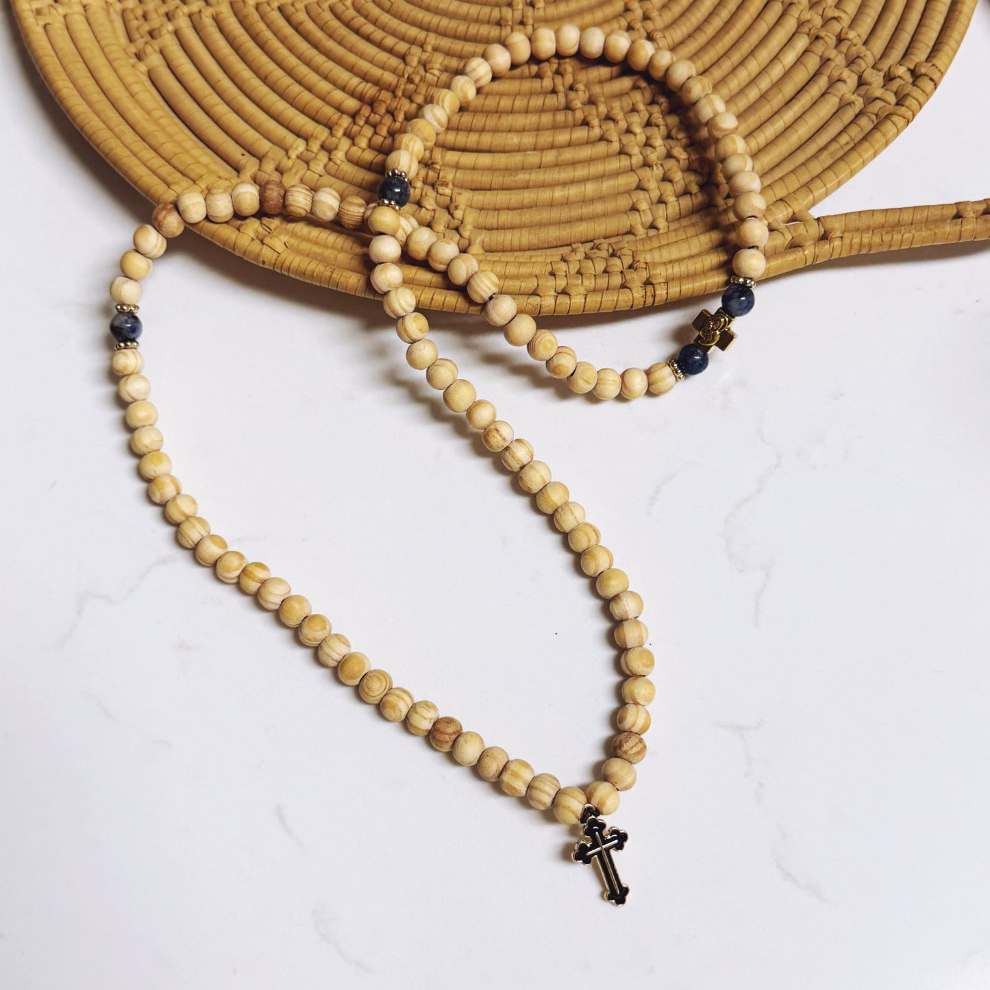 Wooden beaded necklace with a cross pendant on a white surface with a straw hat.